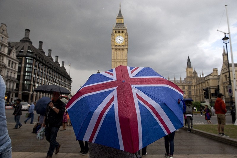  Pedestrian shelters from rain beneath Union flag themed umbrella as they walk near Big Ben clock face and Elizabeth Tower at Houses of Parliament in London on June 25, 2016 (AFP)