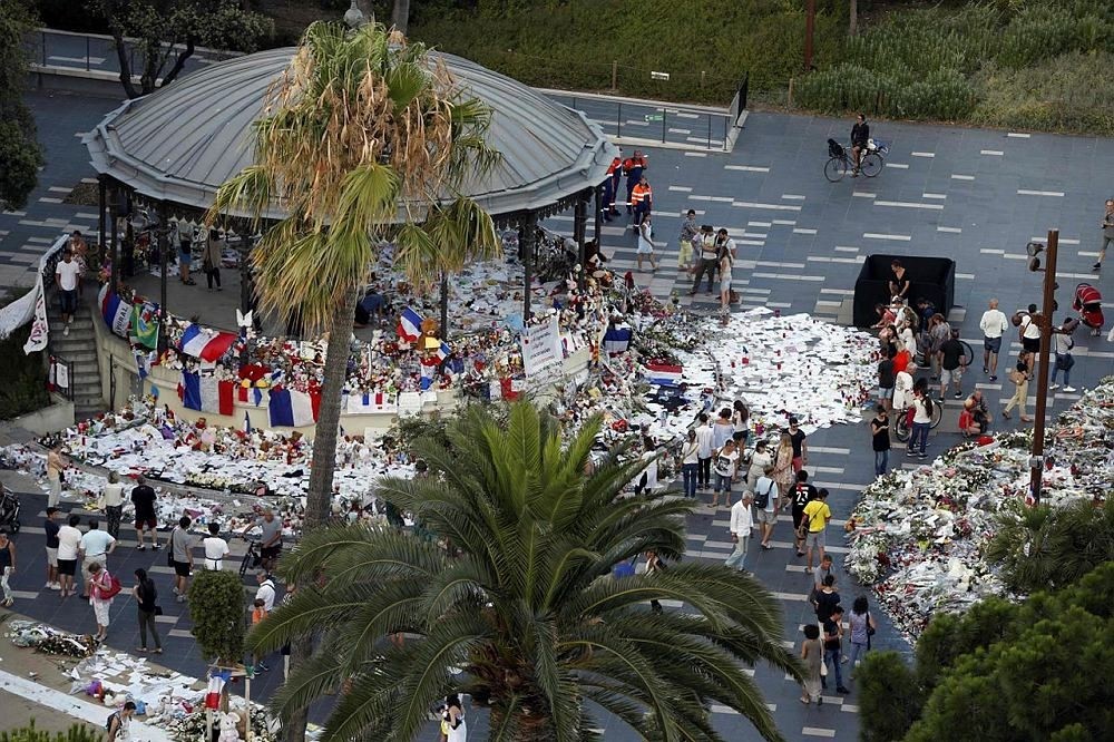 People walk next to floral tributes, notes and candles placed in the road for victims of the deadly Bastille Day attack, on July 20, 2016 in Nice, southern France.  (AFP Photo)