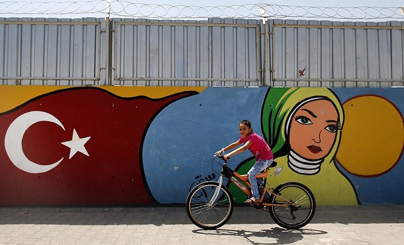 A child cycles past graffiti at the u00d6ncu00fcpu0131nar camp for Syrian refugees next to the border crossing with Syria, near the town of Kilis in southeastern Turkey, Monday, June 20, 2016 (AP Photo)