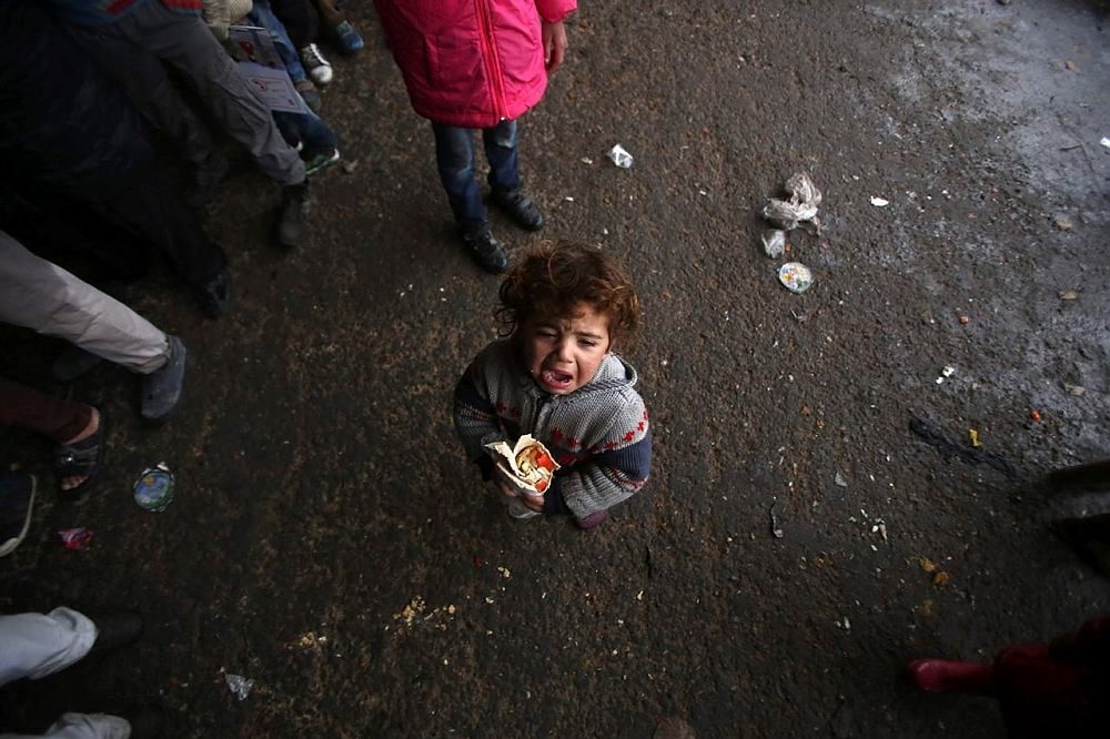 A Syrian child, who fled with his family from rebel-held areas in the city of Aleppo, reacts as he holds a sandwich on December 1, 2016, at a shelter in the neighbourhood of Jibrin, east of Aleppo. (AFP Photo)