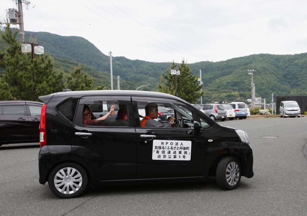 A tourist from Singapore (L), who is the first user of the car sharing service supported by Uber in Kyotango, Japan, waves from the car.