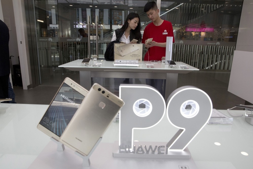 A sales person chats with a customer at a Huawei retail shop with an advertisement for the P9 in Beijing, China.