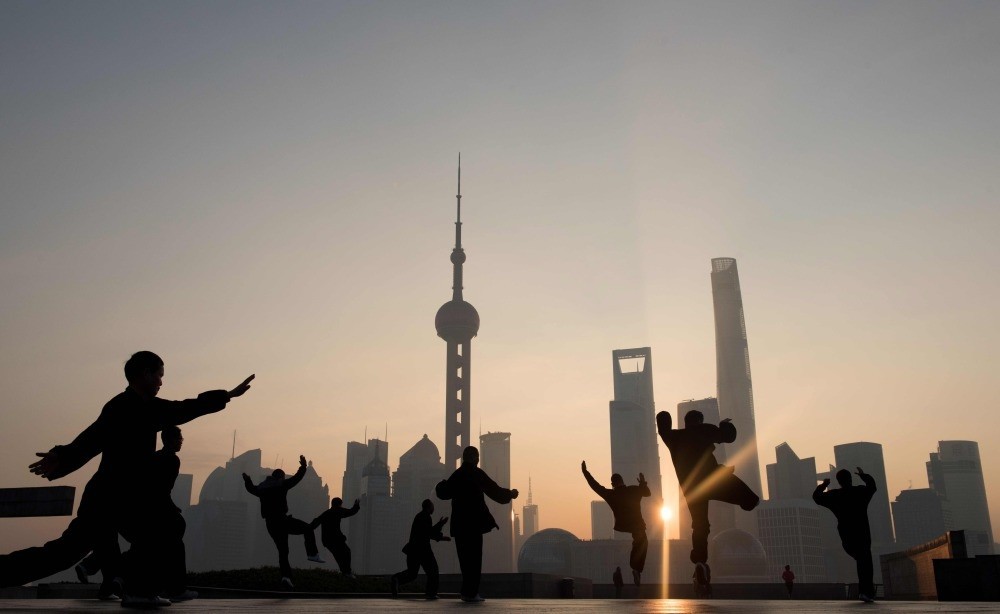 People do morning exercises in front of the skyline of the Lujiazui Financial District in Pudong in Shanghai. 