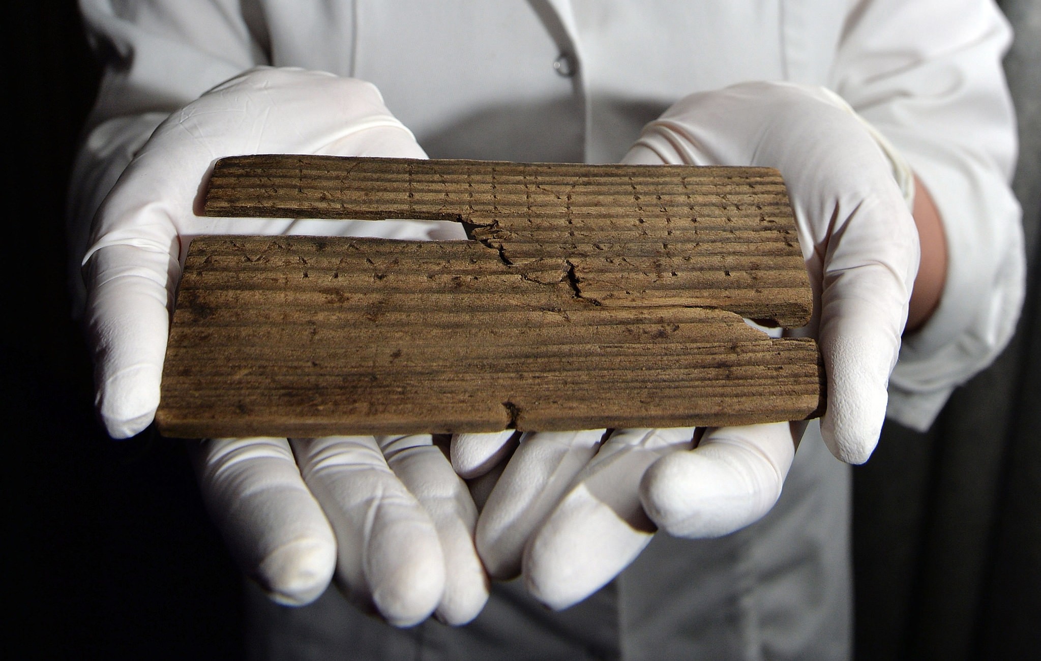 Luisa Duarte, a conservator for the Museum of London, holds a piece of wood with the Roman alphabet written on it in, in London, Wednesday, June 1, 2016 (AP Photo