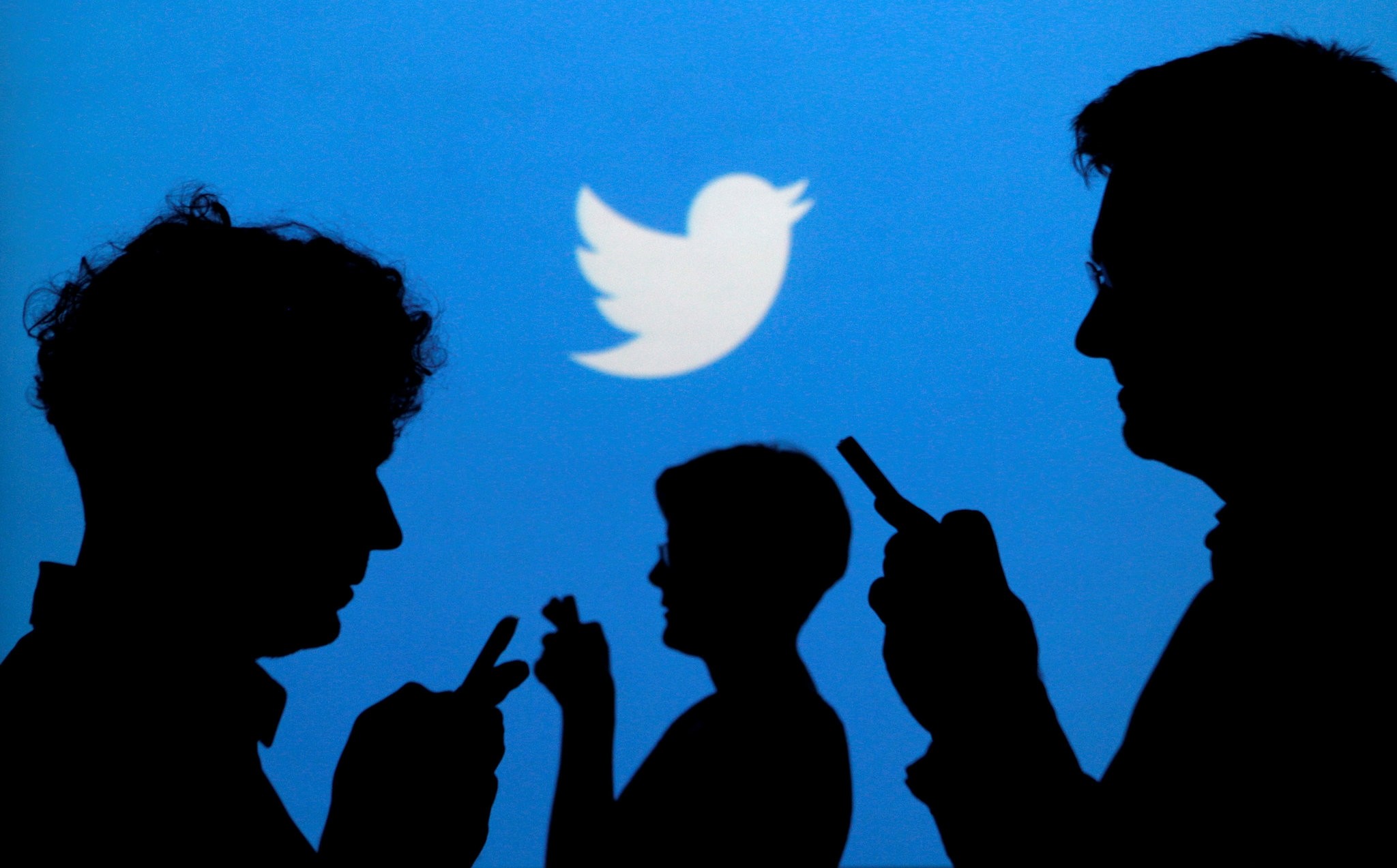 People holding mobile phones are silhouetted against a backdrop projected with the Twitter logo. (Reuters Photo)