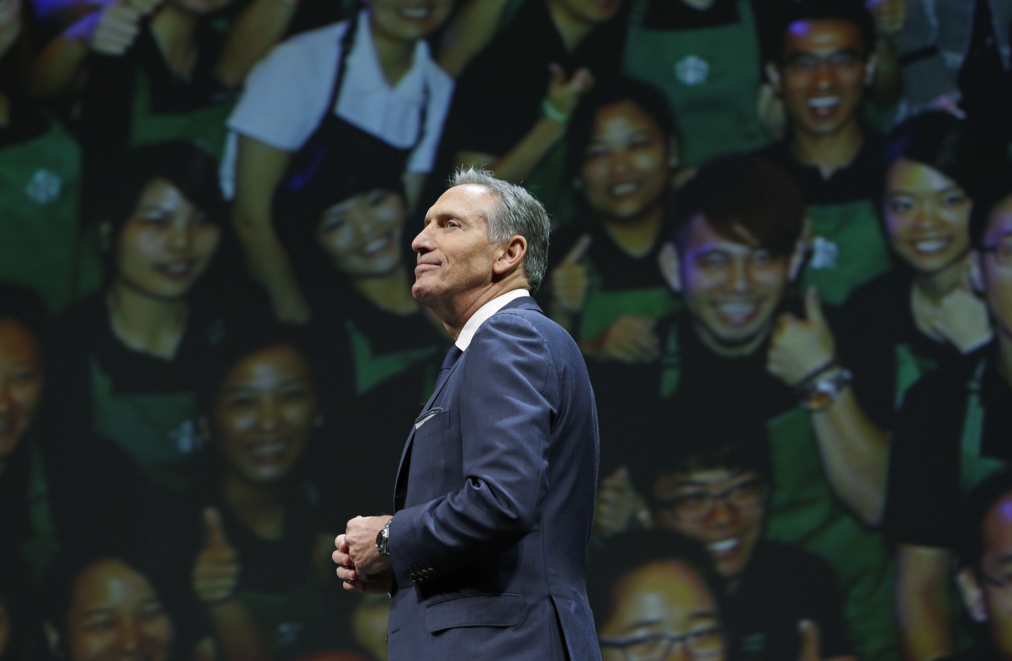 Starbucks CEO Howard Schultz walks in front of a photo of Starbucks baristas, at the coffee company's annual shareholders meeting in Seattle. (AP Photo)