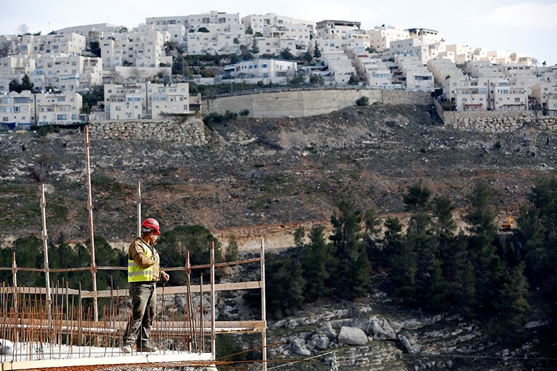 A labourer works at a construction site in the settlement of Ramot, as the Israeli settlement of Ramat Shlomo is seen in the background (Reuters Photo)