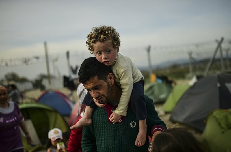 A man carries a child as migrants and refugees carry on with their daily lives at the makeshift camp along the Greek-Macedonian border, on April 1 2016. (AFP Photo)