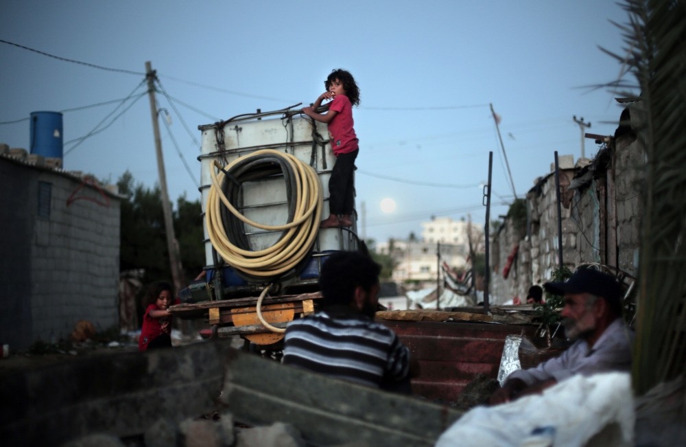 Palestinian children climb on a portable tank used to distribute water in el-Zohor slum, on the outskirts of Khan Younis refugee camp, southern Gaza Strip.