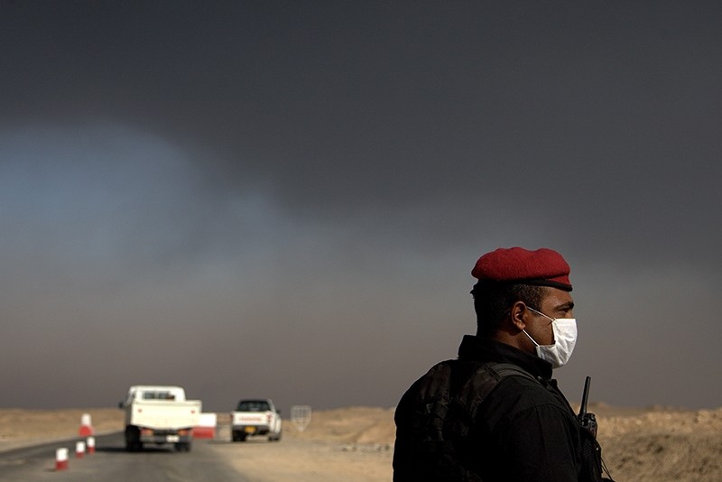 A member of the Iraqi special forces guards a checkpoint near the village of Awsaja, Iraq, as smoke from fires lit by Daesh at oil wells and a sulfur plant fill the air on Saturday, Oct. 22, 2016. (AP Photo)