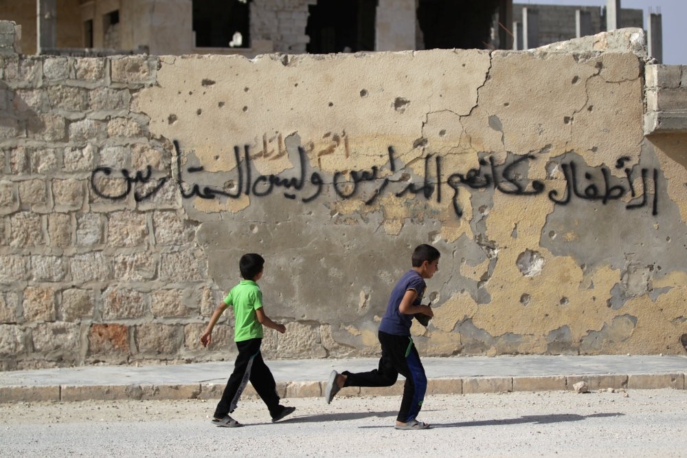 Boys run near graffiti on a riddled wall, in the opposition-controlled area of Maaret al-Numan town in Idlib province on May 26. The graffiti reads in Arabic: ,Children should be placed in schools, not barricades.,