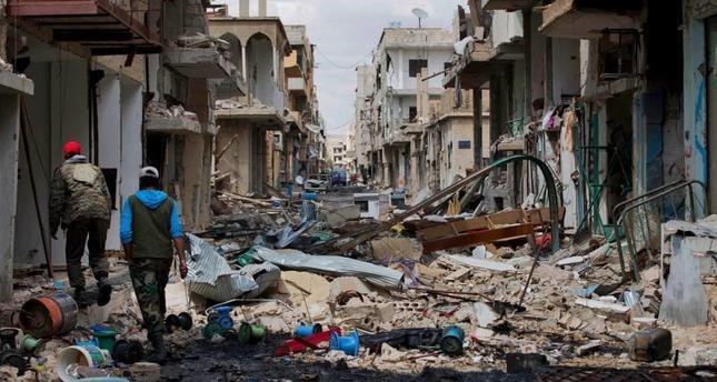 People walk through a devastated part of the town of Palmyra as families load their belongings onto a bus in the central province of Homs, Syria on April 14. (AP Photo)